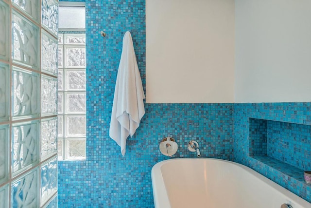 bathroom featuring a wealth of natural light, a bathtub, and tile walls