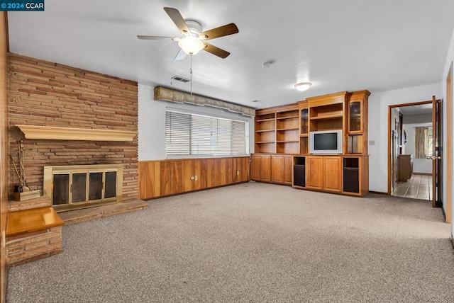 unfurnished living room featuring a fireplace, light colored carpet, and wooden walls