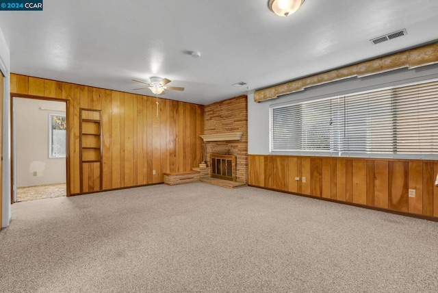 unfurnished living room featuring ceiling fan, a fireplace, wooden walls, and light carpet