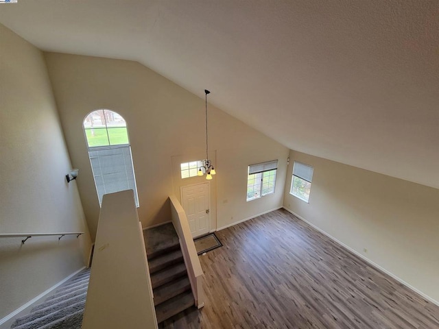 stairway with high vaulted ceiling, wood-type flooring, and a notable chandelier