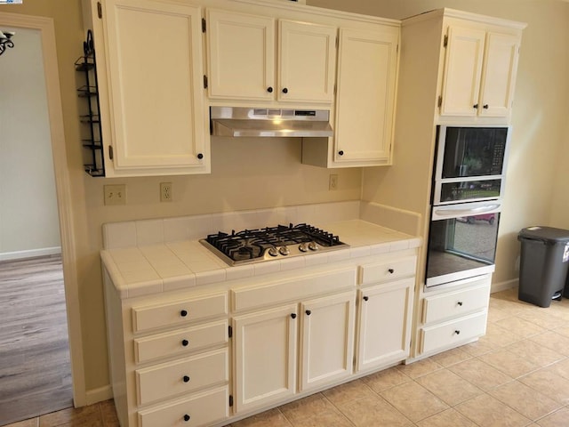 kitchen with tile counters, light tile patterned floors, stainless steel appliances, and extractor fan