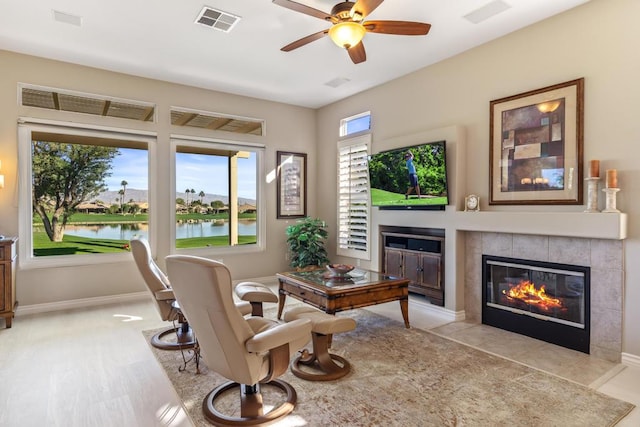 living area featuring ceiling fan, a water view, and a tile fireplace