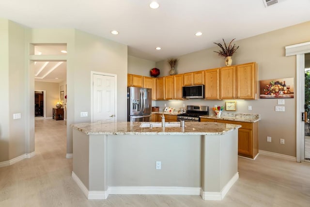 kitchen featuring a center island with sink, sink, light stone countertops, appliances with stainless steel finishes, and light hardwood / wood-style floors