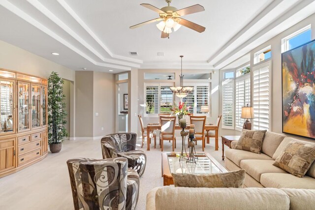 carpeted living room featuring ceiling fan with notable chandelier and a raised ceiling