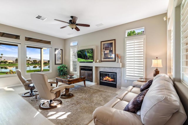 carpeted living room featuring a tile fireplace, a water view, and ceiling fan