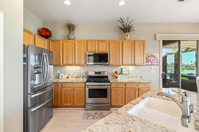 kitchen featuring appliances with stainless steel finishes, light wood-type flooring, light stone counters, and sink