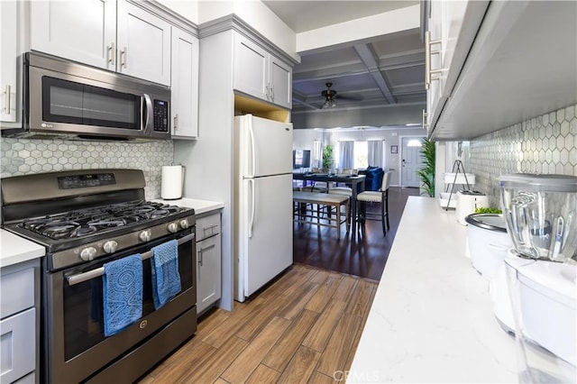 kitchen featuring gray cabinetry, backsplash, coffered ceiling, appliances with stainless steel finishes, and dark hardwood / wood-style flooring