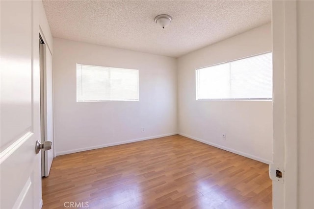 empty room with a wealth of natural light, a textured ceiling, and light wood-type flooring