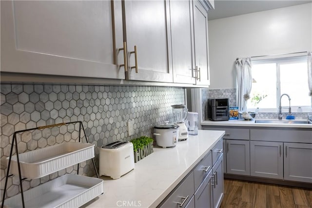 kitchen with tasteful backsplash, gray cabinets, sink, and dark wood-type flooring