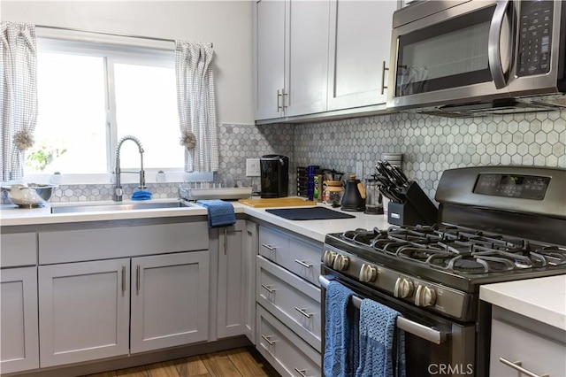 kitchen with sink, decorative backsplash, gray cabinets, light wood-type flooring, and appliances with stainless steel finishes