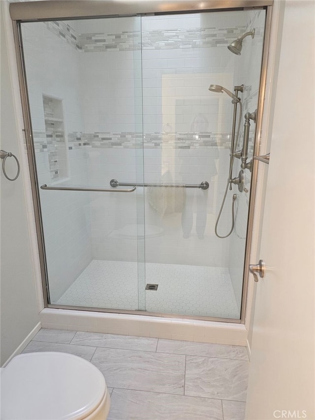 bathroom featuring a shower with door, tile patterned flooring, and toilet