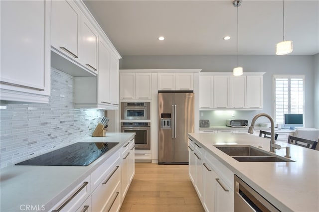 kitchen featuring white cabinetry, sink, stainless steel appliances, decorative light fixtures, and light wood-type flooring