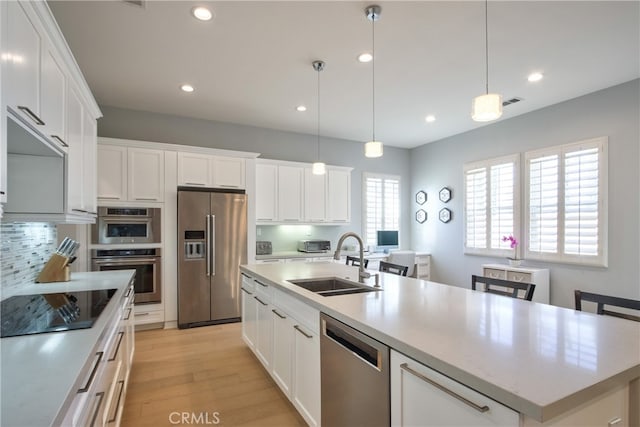 kitchen featuring hanging light fixtures, a center island with sink, white cabinets, and stainless steel appliances