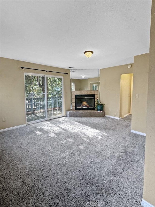 unfurnished living room featuring a tiled fireplace and carpet