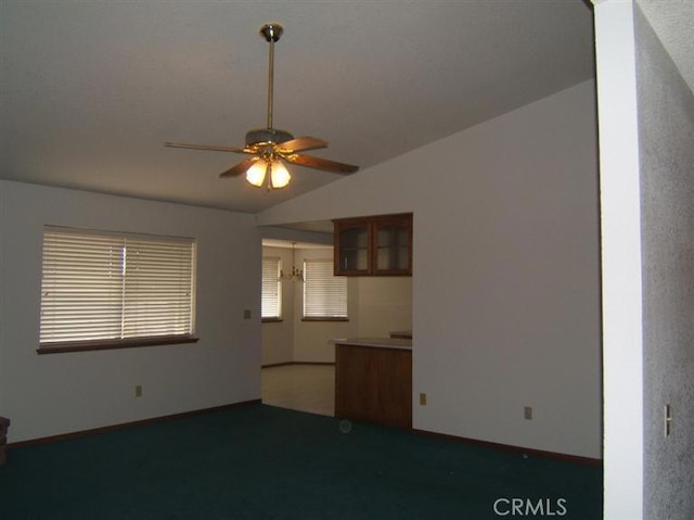 unfurnished living room featuring dark colored carpet, ceiling fan with notable chandelier, and vaulted ceiling