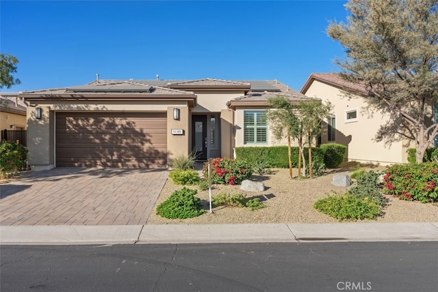 view of front of property with an attached garage, stucco siding, a tile roof, decorative driveway, and roof mounted solar panels