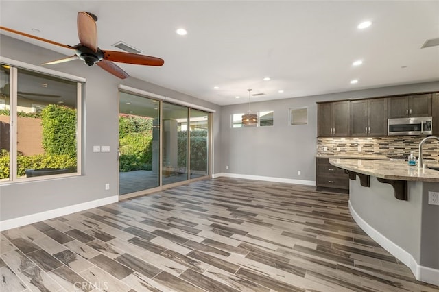 kitchen with hardwood / wood-style floors, hanging light fixtures, light stone counters, dark brown cabinetry, and a breakfast bar area