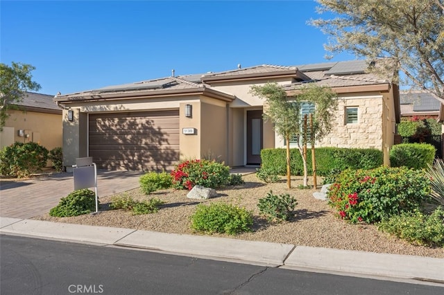 view of front facade featuring stucco siding, solar panels, decorative driveway, and a garage