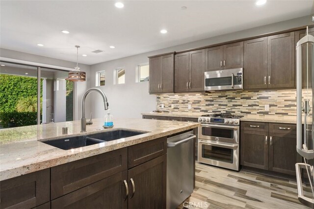 kitchen with appliances with stainless steel finishes, light stone counters, dark brown cabinetry, sink, and hanging light fixtures