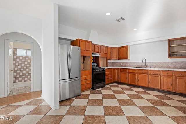 kitchen featuring range with gas stovetop, brown cabinets, freestanding refrigerator, under cabinet range hood, and a sink