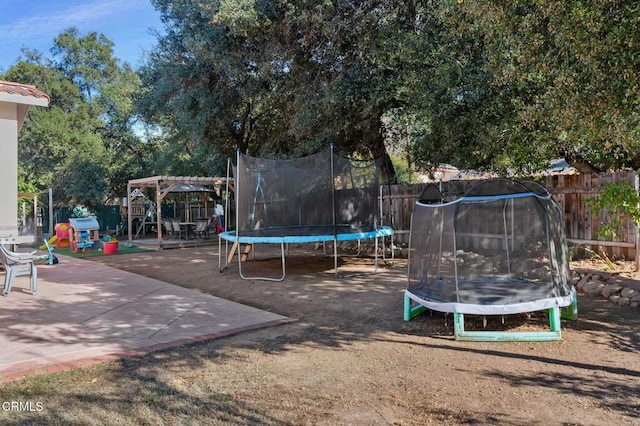 view of playground featuring a trampoline, a patio area, fence, and a pergola