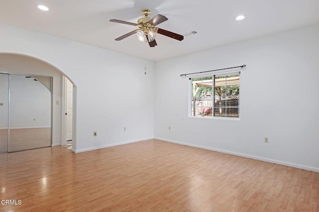 unfurnished room with arched walkways, baseboards, light wood-style flooring, and recessed lighting