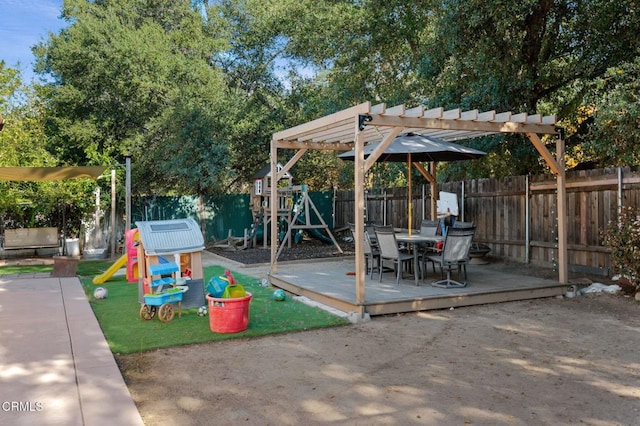 view of playground featuring a deck, a fenced backyard, and a pergola