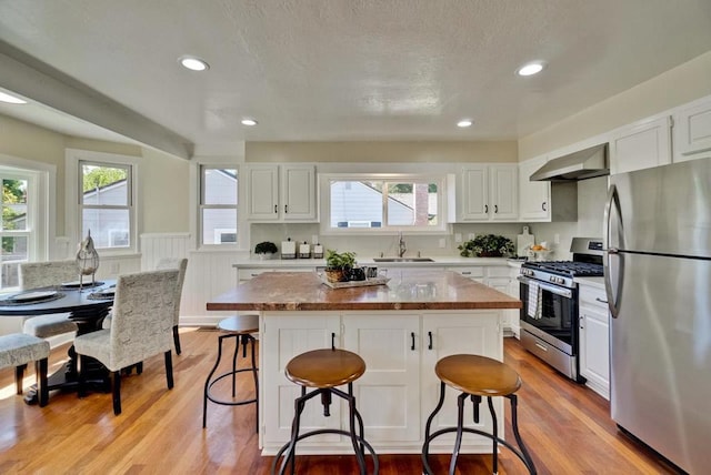 kitchen with wall chimney exhaust hood, white cabinetry, appliances with stainless steel finishes, and a center island