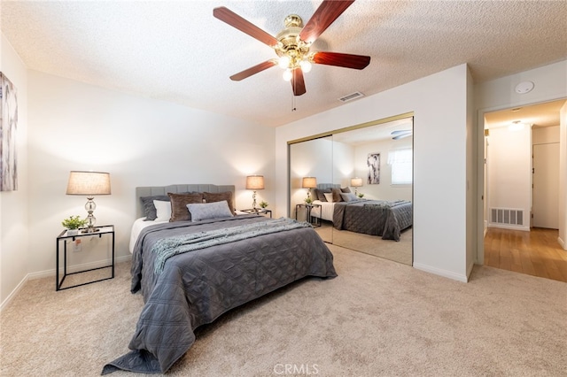 bedroom with a textured ceiling, light carpet, ceiling fan, and a closet