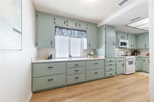 kitchen with white appliances, light hardwood / wood-style flooring, green cabinetry, and a textured ceiling