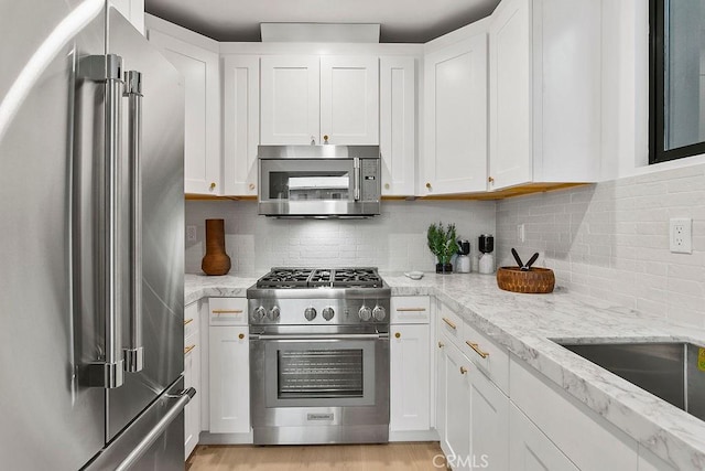 kitchen featuring white cabinetry, light stone counters, high end appliances, and tasteful backsplash