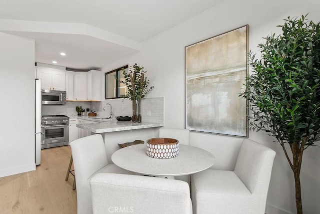 kitchen with light wood-style flooring, a sink, appliances with stainless steel finishes, white cabinetry, and backsplash