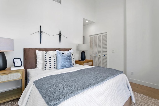 bedroom with visible vents, wood finished floors, a closet, baseboards, and a towering ceiling