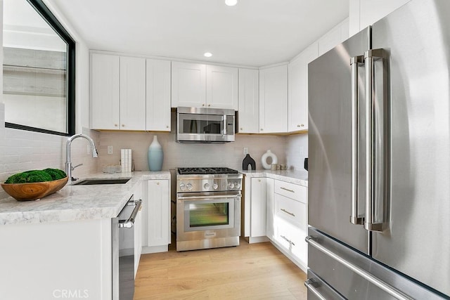 kitchen with tasteful backsplash, light wood-style floors, white cabinets, high end appliances, and a sink