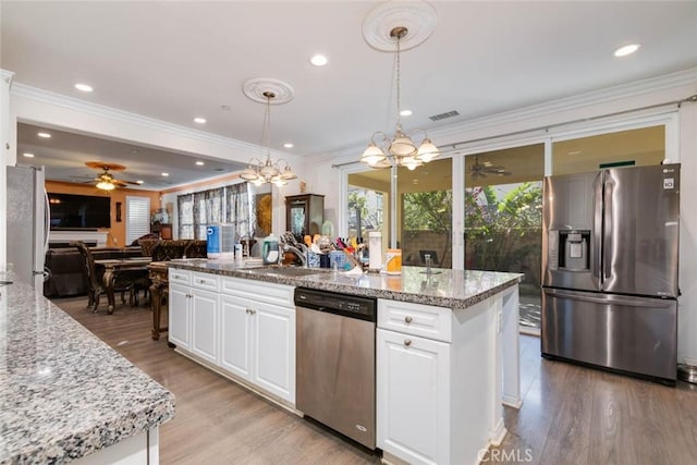 kitchen with light stone countertops, appliances with stainless steel finishes, light wood-type flooring, white cabinetry, and hanging light fixtures