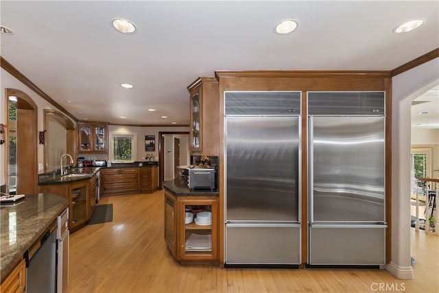 kitchen featuring sink, light hardwood / wood-style flooring, ornamental molding, built in refrigerator, and dark stone counters