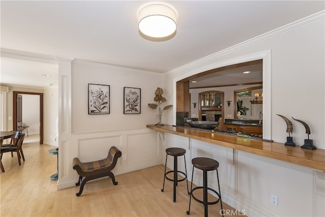 kitchen with a kitchen bar, sink, black gas cooktop, ornamental molding, and light hardwood / wood-style flooring