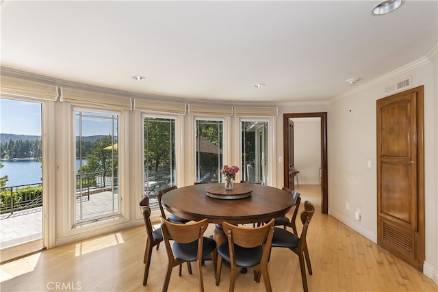 dining area featuring a water view, light wood-type flooring, and crown molding