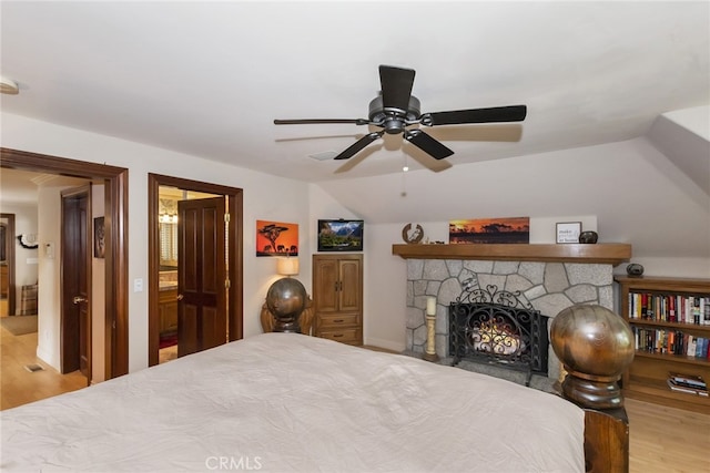 bedroom featuring ceiling fan, vaulted ceiling, light wood-type flooring, and a fireplace