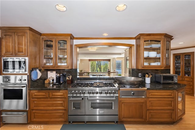 kitchen with light hardwood / wood-style floors, stainless steel appliances, decorative backsplash, dark stone counters, and ornamental molding