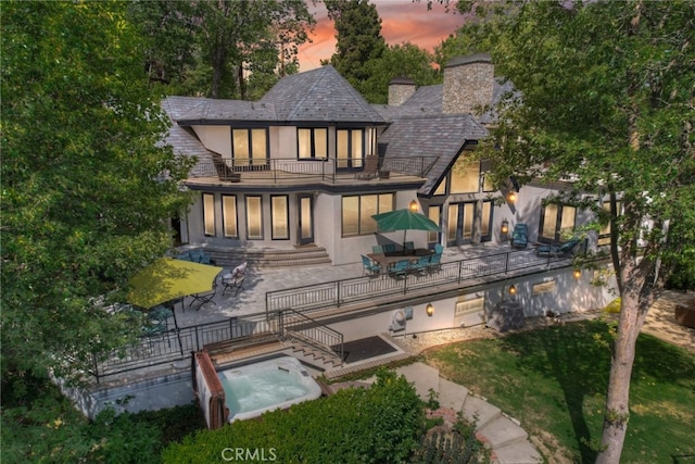 back house at dusk featuring a balcony, a jacuzzi, and a patio