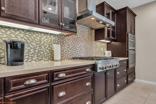 kitchen with wall chimney exhaust hood, stainless steel appliances, decorative backsplash, dark brown cabinets, and light tile patterned flooring