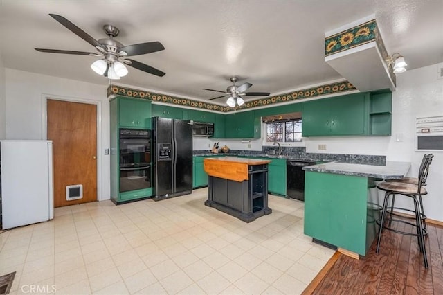 kitchen featuring black appliances, ceiling fan, light wood-type flooring, a kitchen island, and a kitchen bar