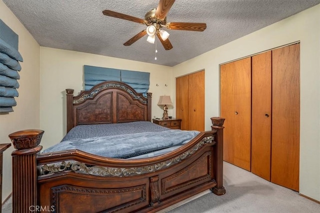 bedroom featuring two closets, a textured ceiling, light colored carpet, and ceiling fan