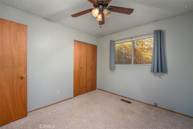 unfurnished bedroom with a textured ceiling, ceiling fan, light carpet, and a closet