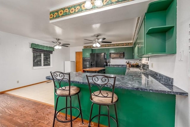 kitchen with hardwood / wood-style floors, black appliances, green cabinets, sink, and kitchen peninsula