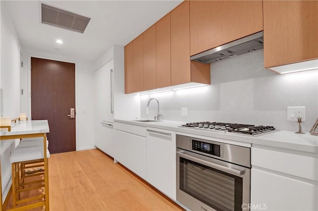 kitchen with stainless steel appliances, sink, exhaust hood, light hardwood / wood-style floors, and white cabinetry