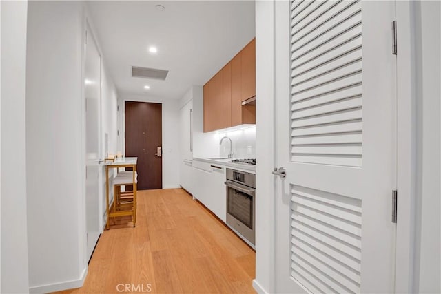 kitchen featuring sink, white gas stovetop, light hardwood / wood-style flooring, and stainless steel oven