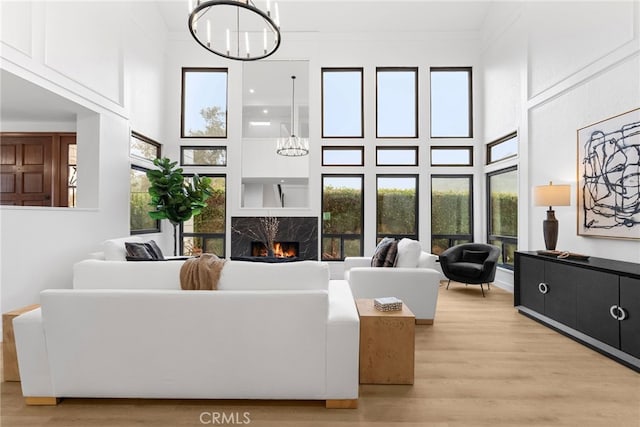 living room with a high ceiling, light hardwood / wood-style flooring, a high end fireplace, crown molding, and a chandelier