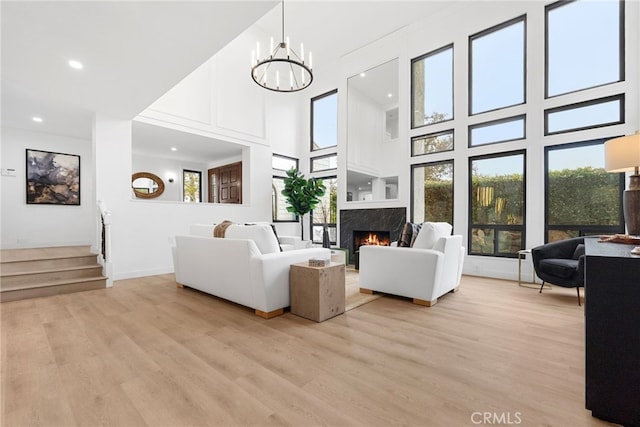 living room with a notable chandelier, a premium fireplace, a high ceiling, and light hardwood / wood-style flooring